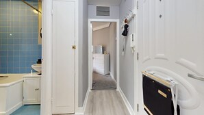A narrow hallway with a white door on the left, a vanity with a mirror and sink on the right, and a coat rack with an umbrella. - Bright 1Bedroom Home-Brixton Tube 12min Away (Brixton)