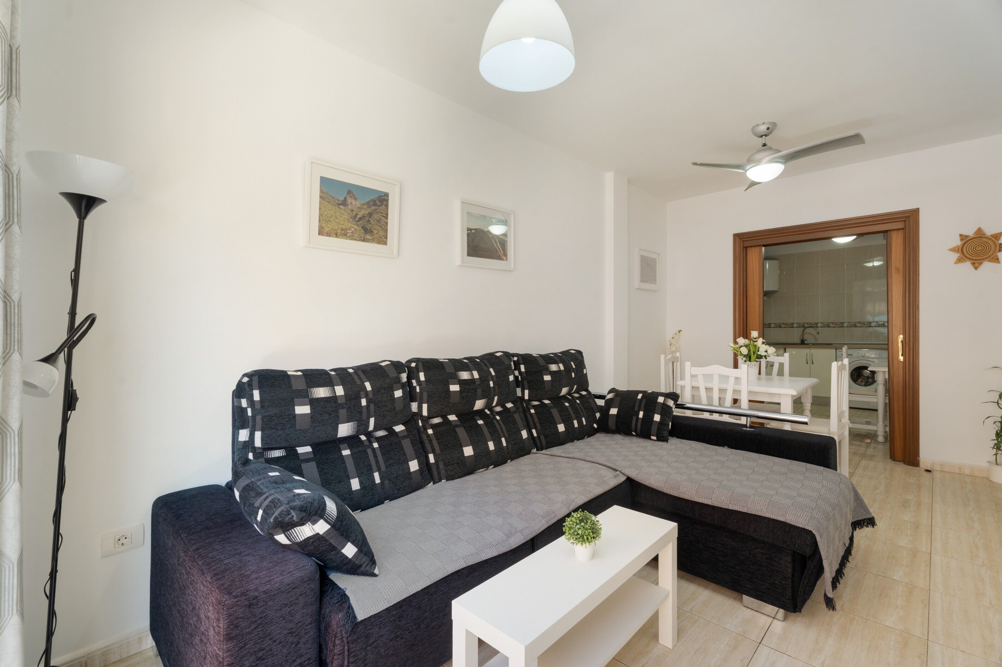 Una sala moderna con un sofá seccional, una mesa de centro blanca y un ventilador de techo.