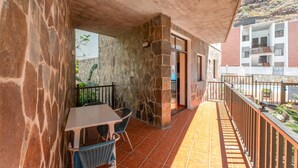 A balcony with stone walls, a table, chairs, and a view of a building and landscape. - Casa Carolina 2 – Cozy Home Steps from the Sea in Playa de Santiago (Playa de Santiago)