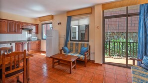 A kitchen with wooden cabinets, a dining table, and a sofa with patterned cushions. - Casa Carolina 2 – Cozy Home Steps from the Sea in Playa de Santiago (Playa de Santiago)