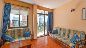 A living room with two patterned sofas, a wooden bench, and a sliding glass door leading to a balcony. - Casa Carolina 2 – Cozy Home Steps from the Sea in Playa de Santiago (Playa de Santiago)