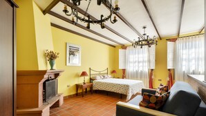 A room with a bed, a sofa, a fireplace, a chandelier, and a window with curtains.