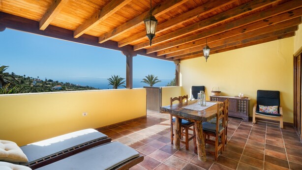 A covered patio with a wooden ceiling, a dining table, chairs, and a view of the ocean.