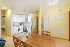 Une cuisine compacte équipée d’un lave-linge, d’un four et d’un réfrigérateur. On y trouve une table à manger avec des chaises et deux verres à vin.