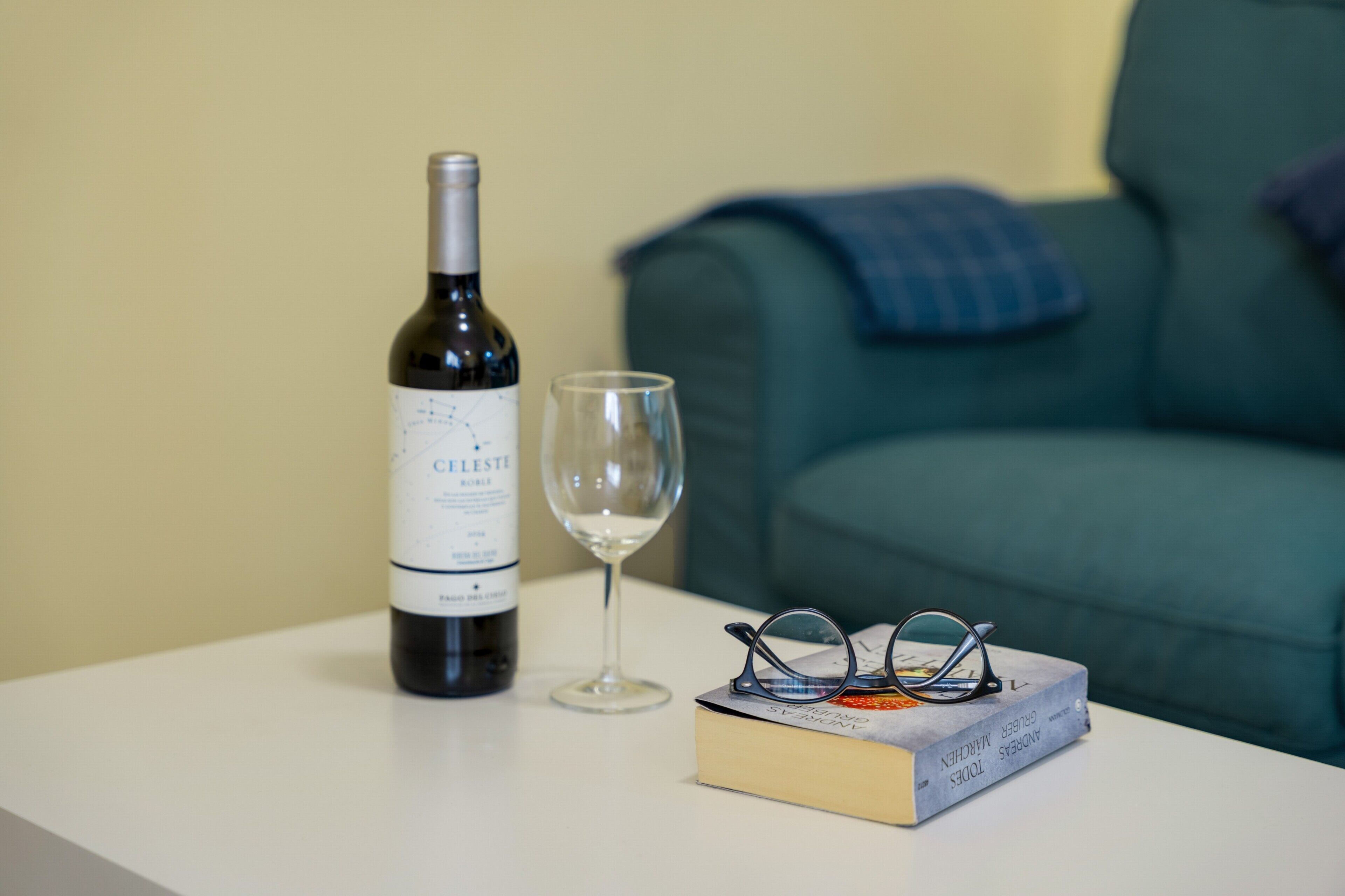 A bottle of Celeste wine, a wine glass, and a book with glasses on a table.