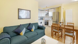 Una sala de estar con un sofá, una mesa de comedor con sillas, una cocina equipada y un cuadro en la pared.