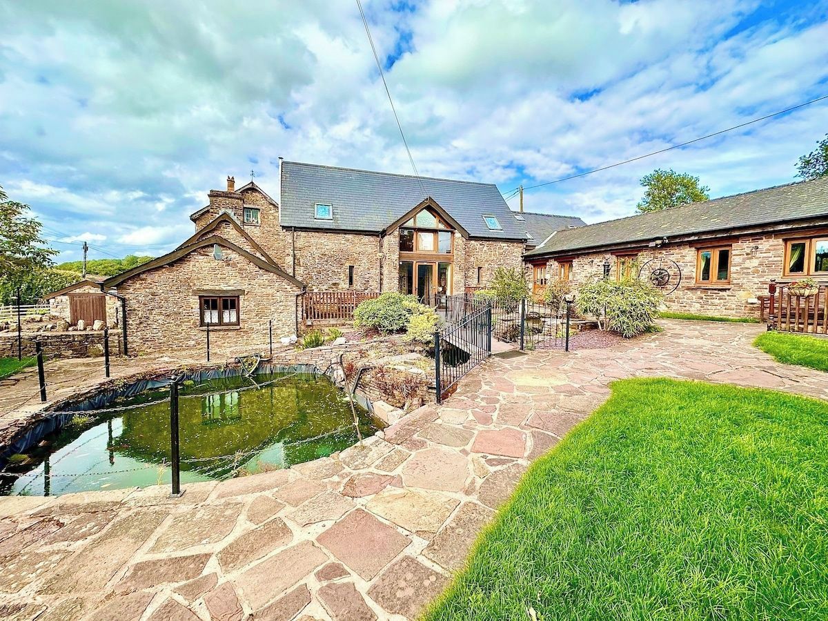 A stone building with a pond, a stone pathway, and a grassy area.