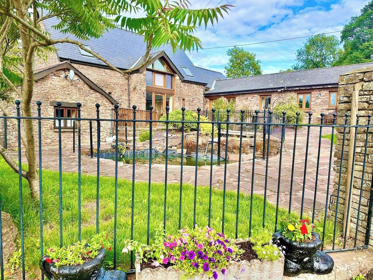 A stone building with a fenced yard, a pond, and flower beds.