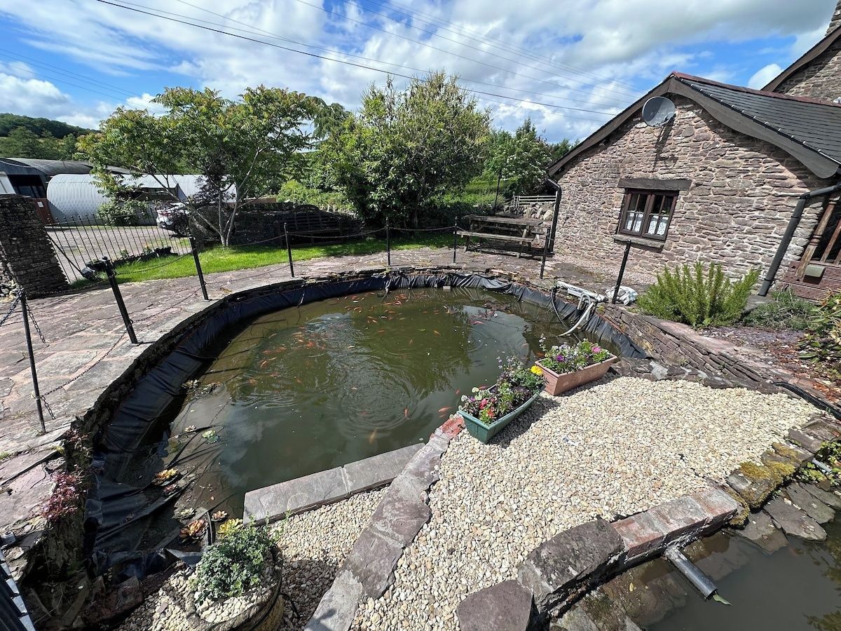 A pond with a stone wall, a small house, and a garden area with plants.
