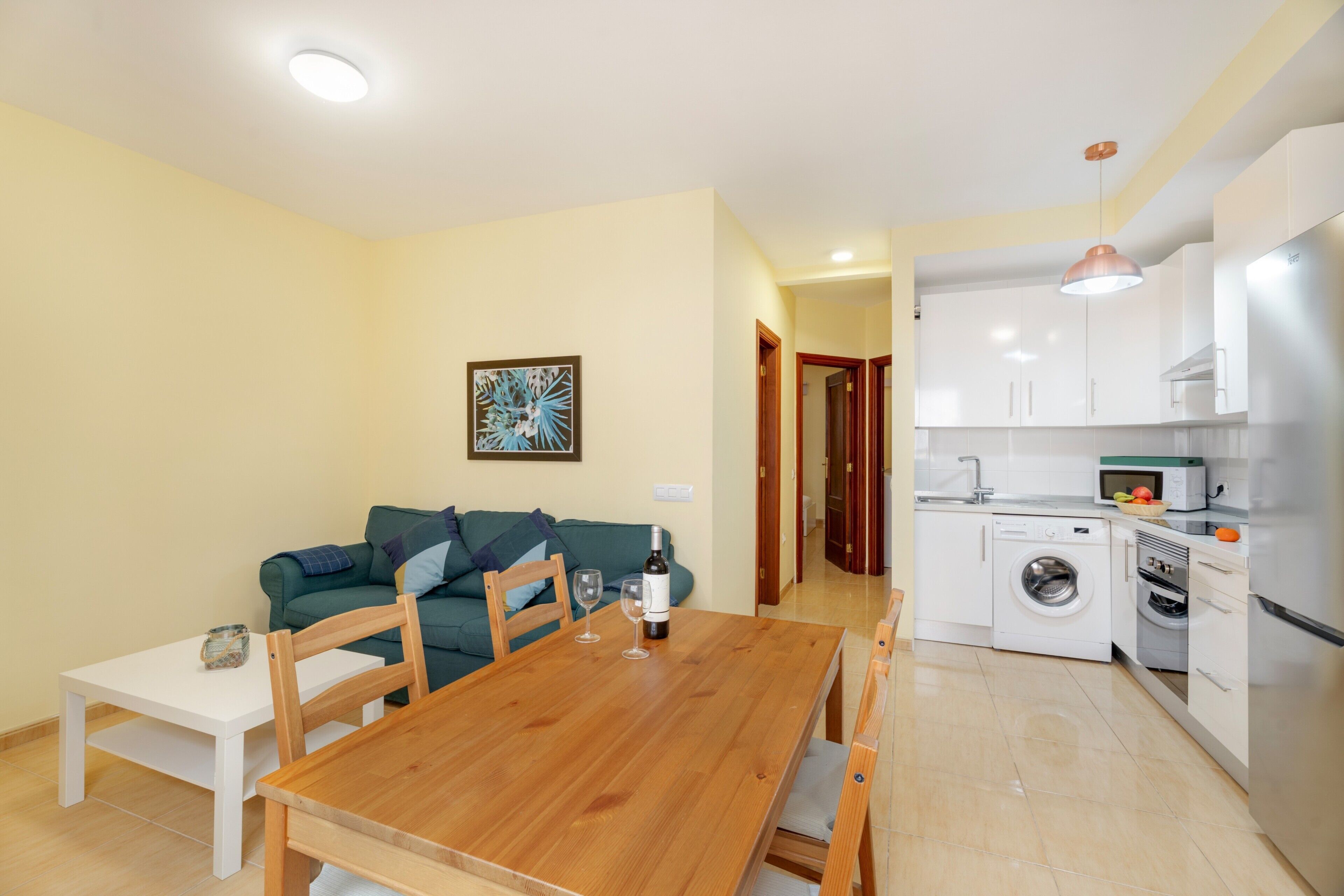Un espacio habitable compacto con una mesa de comedor, un sofá, una cocina equipada con lavadora e iluminación en el techo.