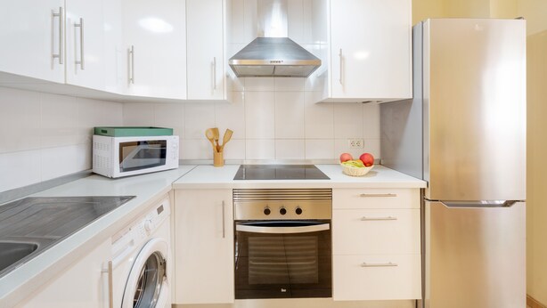 Una cocina moderna con gabinetes blancos, una campana extractora de acero inoxidable, horno empotrado, microondas y refrigerador.