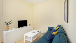 Una sala de estar con un sofá blanco, un televisor de pantalla plana, una mesita de centro blanca y un cuadro en la pared.
