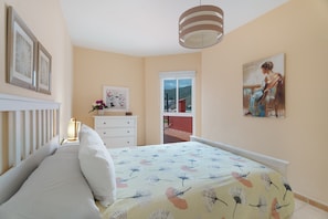 Un dormitorio con cama, cómoda, ventana y un cuadro en la pared.