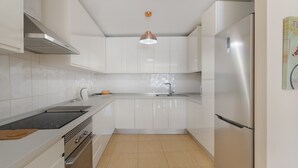 Eine moderne Küche mit weißen Schränken, einem Edelstahlkühlschrank, einem Einbauofen und einer Pendelleuchte.