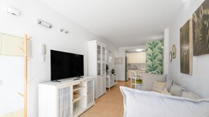 A modern living room with a flat-screen TV, white cabinetry, a sofa, and a dining area with a green wall.