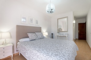Une chambre à coucher comprenant un lit, des lampes de chevet, une table de chevet, une commode, un miroir et un lustre.