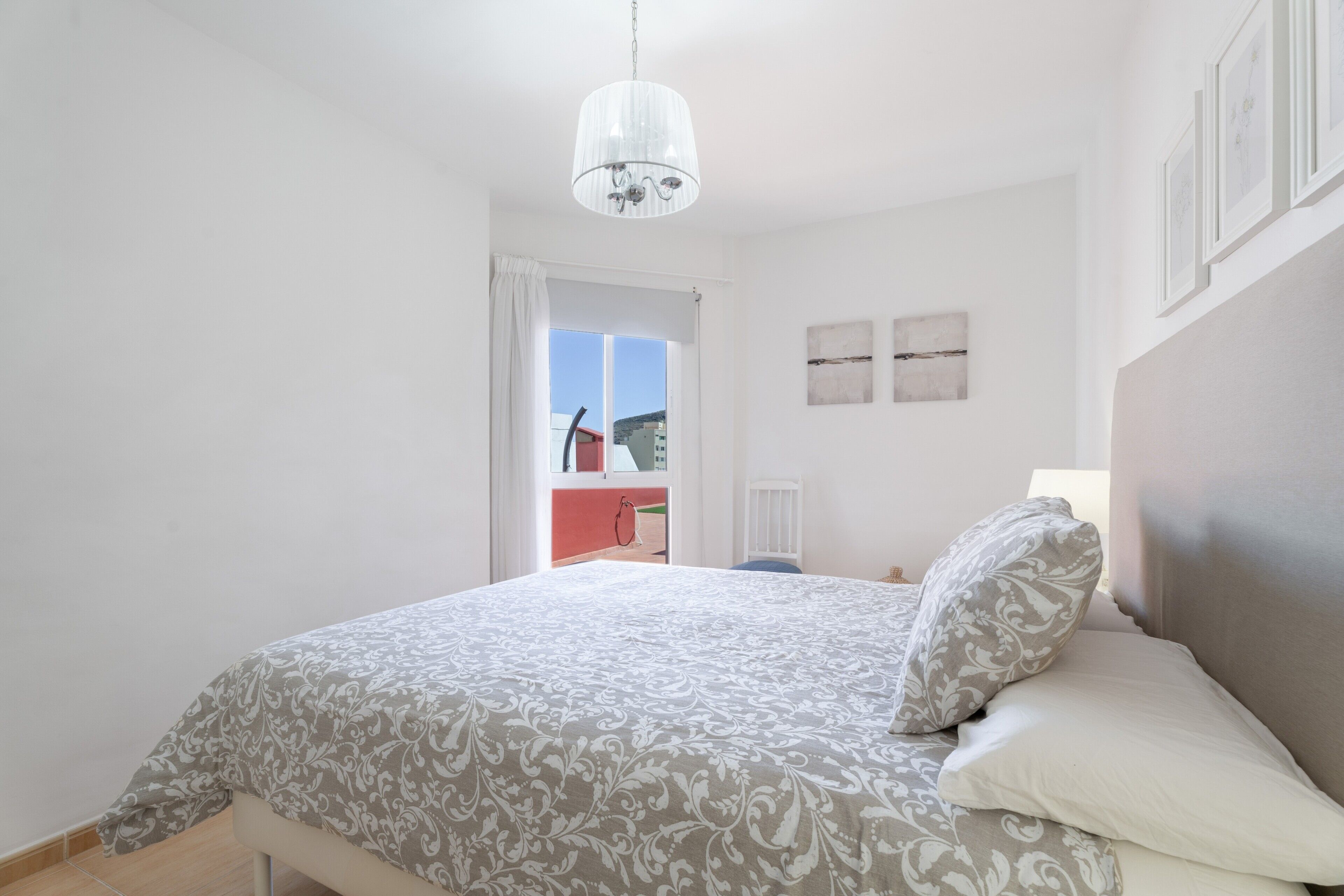 Une chambre à coucher avec un lit, un lustre, une fenêtre et une vue sur l’extérieur.
