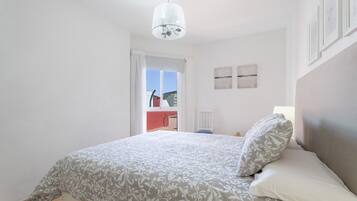 Une chambre à coucher avec un lit, un lustre, une fenêtre et une vue sur l’extérieur.