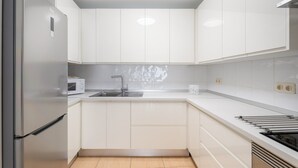 A modern kitchen with white cabinets, a stainless steel refrigerator, a microwave, and a stove.