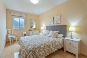 Une chambre à coucher comprenant un lit, des tables de chevet, une chaise, une fenêtre donnant sur un beau paysage et des œuvres d’art accrochées au mur.