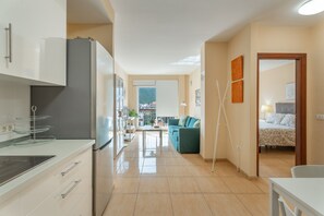 Una cocina moderna con refrigerador, estufa y comedor. Hay un sofá y una cama en la sala.
