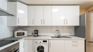 Una cuina moderna amb armaris blancs, microones integrat, cafetera, rentadora i nevera d'acer inoxidable.
