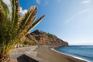 Una playa con un acantilado rocoso, palmeras y un cielo despejado.