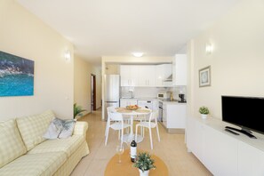 Un salon moderne comprenant un canapé, une table à manger avec des chaises, un coin cuisine avec des placards, un téléviseur et un tableau accroché au mur.
