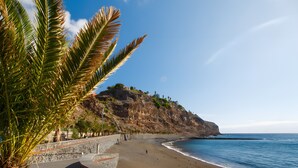 Una playa con un acantilado rocoso, palmeras y cielo despejado.