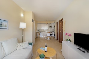 A living room with a sofa, a coffee table with a bottle and glass, a TV on a stand, and a kitchen in the background. - Casa Miramar 2 – Comfort and Unbeatable Location in the Heart of San Sebastián (San Sebastian de La Gomera)