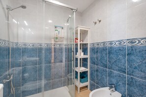 A bathroom with a glass shower enclosure, a white sink, and a blue tiled wall with a decorative border. - Casa Miramar 2 – Comfort and Unbeatable Location in the Heart of San Sebastián (San Sebastian de La Gomera)
