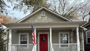Een twee verdiepingen tellend huis met een rode deur, witte hekwerken en een Amerikaanse vlag.