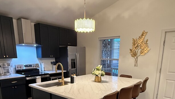 Een moderne keuken met donkere kasten, een centraal eiland met barkrukken, een roestvrijstalen koelkast en een hanglamp.