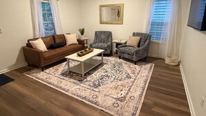 Een woonkamer met een bruine bank, gestreepe fauteuils, een salontafel en een groot vloerkleed.