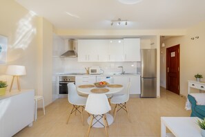 Une cuisine moderne avec des meubles blancs, un réfrigérateur en acier inoxydable et une table à manger avec quatre chaises.