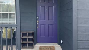 A house with a purple front door, a small porch with a bench, and a doormat.