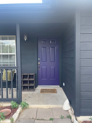 A house with a purple front door, a small porch with a bench, and a doormat.