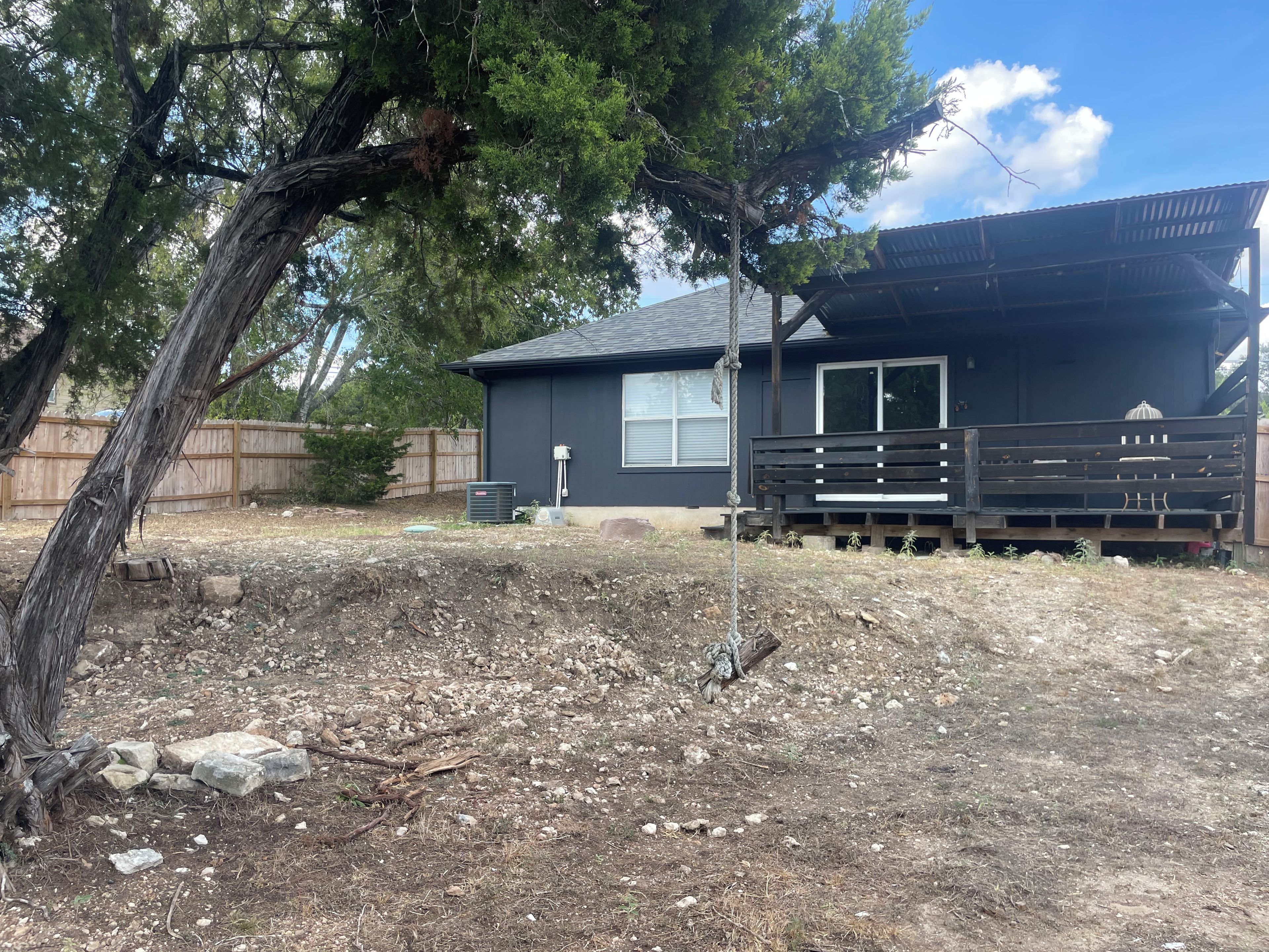 A residential property with a fenced yard, a wooden deck, and a house with a dark exterior.