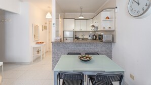 Een moderne keuken met granieten aanrecht, een eettafel met stoelen, een grote wandklok en een plantje op het buffet.