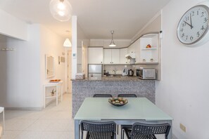 Una cucina moderna con piani di lavoro in granito, un tavolo da pranzo con sedie, un grande orologio a parete e una piccola pianta sul mobiletto.