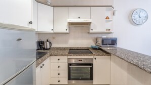 Een kleine keuken met een inbouwoven, magnetron en een klok aan de muur.