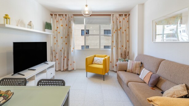 Een woonkamer met een bank, fauteuil, televisie en een eethoek met stoelen.