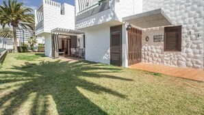Un edificio moderno, bianco, con un patio, un'area salotto coperta e un muro in pietra.