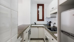 Una cucina compatta con pensili bianchi, un piano di lavoro in granito, un lavello incassato, una macchina da caffè e un frigorifero.