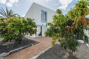 A modern house with a white exterior and blue trim, surrounded by well-maintained gardens and a gravel pathway.