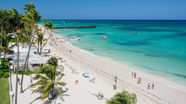 A beach with clear turquoise waters, palm trees, and a pier. - Private Beach | Terrace and Pool • Fast WiFi (Punta Cana)