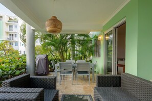 A covered patio area with a table and chairs, surrounded by greenery and a view of a building. - Private Beach | Terrace and Pool • Fast WiFi (Punta Cana)