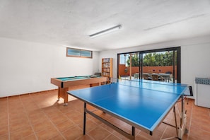 A room with a pool table, a ping pong table, a bookshelf, and a sliding glass door leading to an outdoor area.