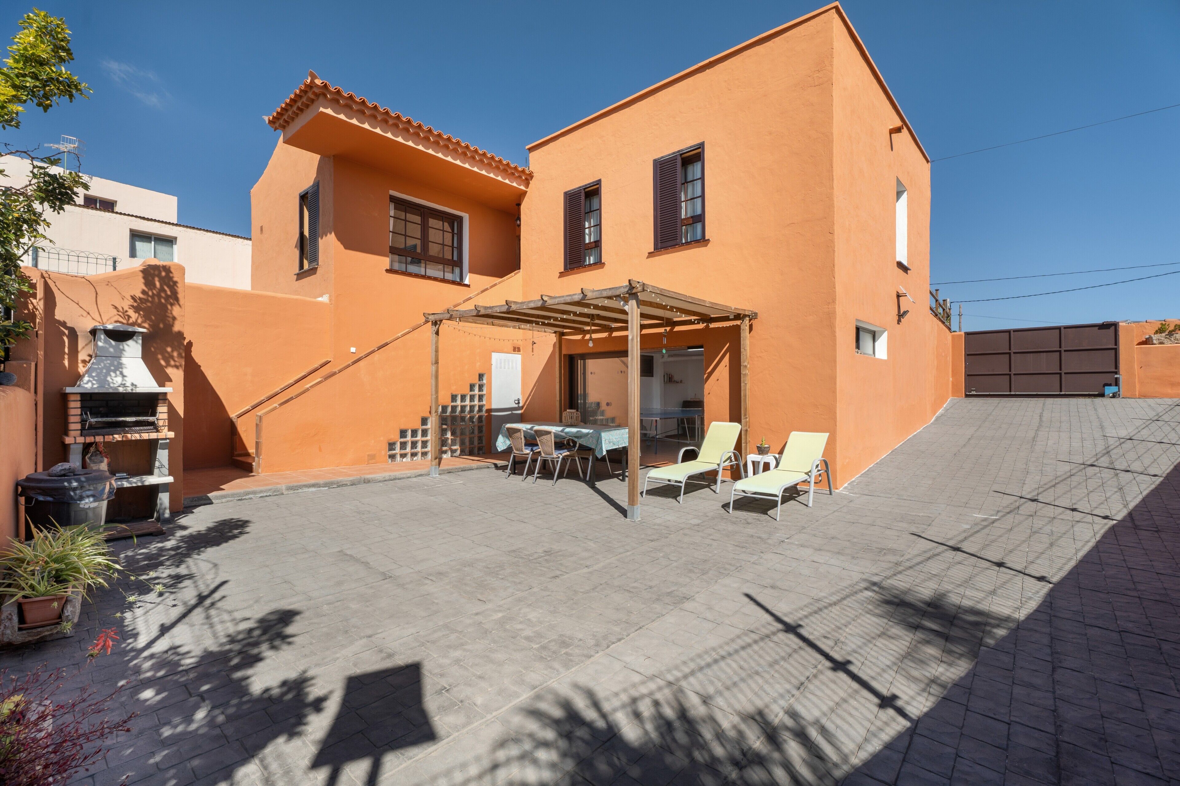 Un bâtiment à deux étages doté d’un patio comprenant un barbecue, des sièges d’extérieur et une pergola.