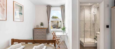 A bedroom with a bed, a desk, a dresser, and a shower area.